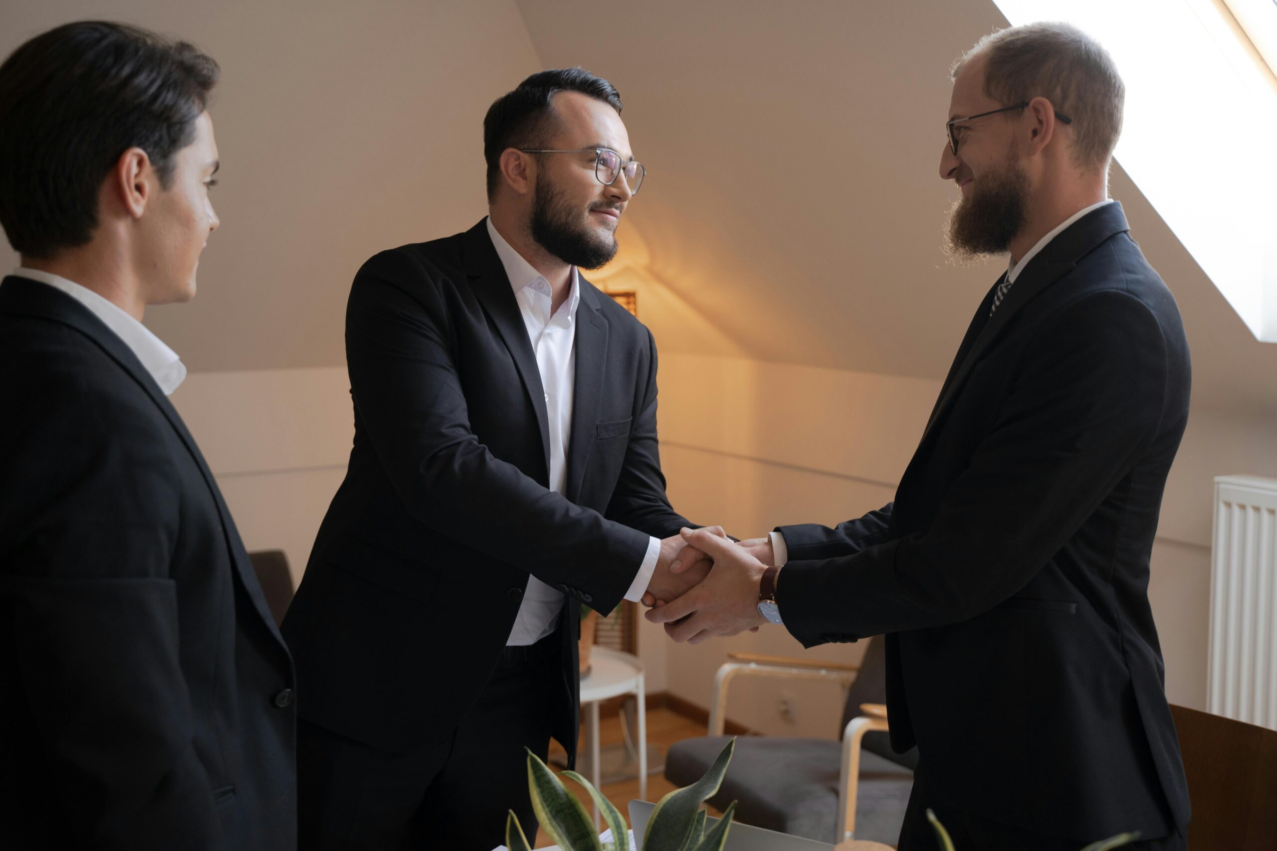 Three businessmen shaking hands in a professional indoor meeting, symbolizing partnership and agreement.