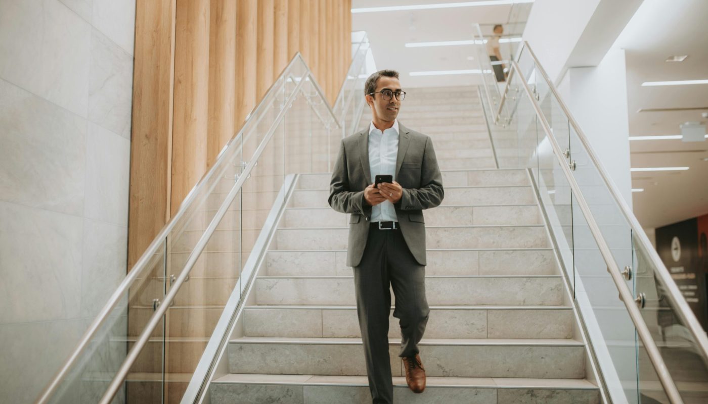 Confident businessman in suit walking downstairs while using a smartphone.